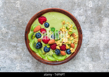 Frullato Verde matcha tea ciotola con frutti, bacche, granola, noci e semi. sana colazione vegan. vista superiore Foto Stock