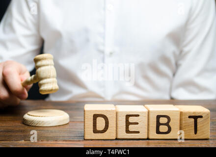 Blocchi di legno con la parola debito e giudicare con un martello. Il concetto di cooperazione giudiziaria la punizione per il mancato pagamento del debito. Proprietà dei debiti. Evasione fiscale / avo Foto Stock