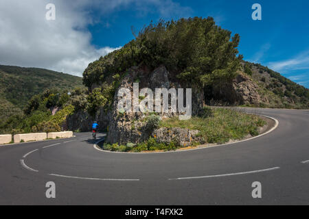Drammatica vista di un ciclista su strada in bicicletta pedalando un tornante nel Parque Rural de Anaga park, TF-12 Tenerife, Spagna Foto Stock