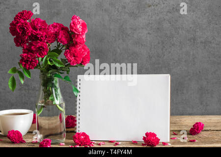 Bigliettino vuoto e rose fiori con tazza di tè su tavola in legno rustico. mock up. matrimonio o womens giorno concetto. still life Foto Stock