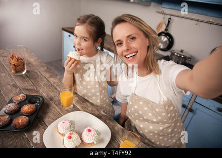 Felice famiglia amorevole in cucina. La madre e il bambino figlia ragazza stanno mangiando i cookie che hanno reso e divertirsi in cucina. Cibo fatto in casa Foto Stock
