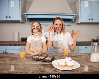 Felice famiglia amorevole in cucina. La madre e il bambino figlia ragazza stanno mangiando i cookie che hanno reso e divertirsi in cucina facendo facce buffe. Foto Stock