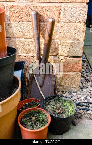 Un paio di piccola mano badili puntellato contro un muro di casa con alcuni vasi per piante in una zona residenziale giardino sul retro. Foto Stock