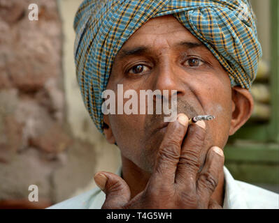 Di mezza età uomo indiano con turbante fuma una economici Indian mini-sigaro (beedi). Foto Stock