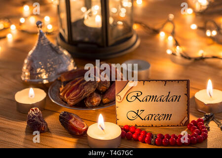 Biglietto di auguri Ramadan Kareem con date, rosario, candele in marrone tavolo in legno Foto Stock