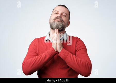 Speranzoso coppia uomo caucasico in maglione rosso a unirvi nella preghiera ringraziando per chiedere migliori. Il marito pregare o sperare. Concetto di fede Foto Stock