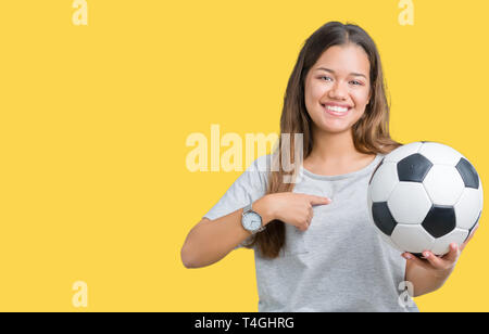 Giovane bella bruna donna azienda soccer football palla su sfondo isolato con sorpresa faccia puntare il dito a se stesso Foto Stock