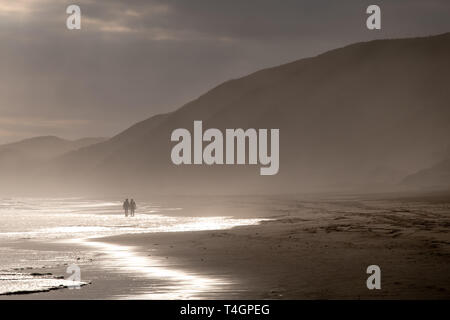 La gente camminare alla luce del sole in lontananza sulla spiaggia sabbiosa a Brenton sul mare, fotografata al tramonto. Knysna, Sud Africa. Foto Stock