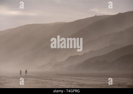 Sagome di persone in lontananza camminando sulla spiaggia sabbiosa a Brenton sul mare, fotografata al tramonto. Knysna, Sud Africa. Foto Stock