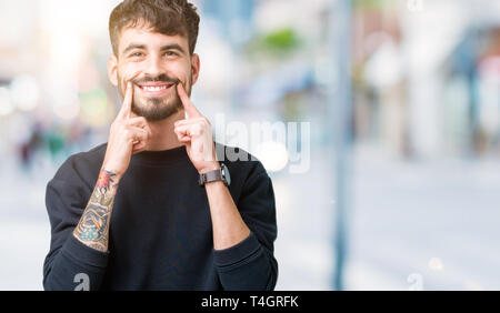 Giovane uomo bello su sfondo isolato sorridente con la bocca aperta, le punte delle dita rivolte e costringendo il sorriso allegro Foto Stock