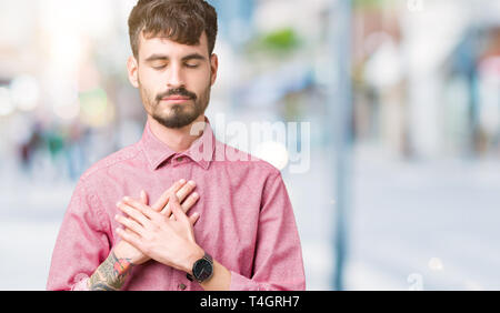 Giovane uomo bello indossare maglia rosa su sfondo isolato sorridente con le mani sul petto con gli occhi chiusi e grato gesto sul viso. Salute conce Foto Stock