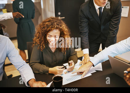 Giovane imprenditrice di ridere mentre si discute di grafici con i colleghi durante una riunione in un ufficio boardroom Foto Stock