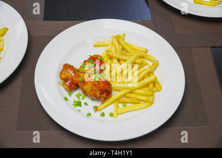 Patate fritte con le cosce di pollo e cipollotti tritati su piastra Foto Stock