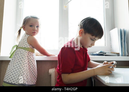 Sorella e fratello sono seduti in cucina e giocare con il telefono Foto Stock