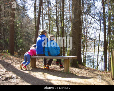 Felice madre con figlio e figlia seduta su una panchina e guardando una bella vista sulla foresta Foto Stock