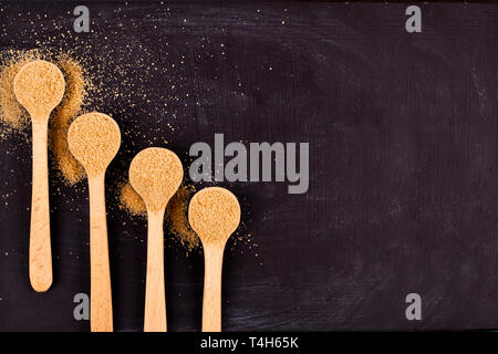 Quattro cucchiai di legno marrone con zucchero di canna su sfondo nero. Vista da sopra con copia spazio. Foto Stock
