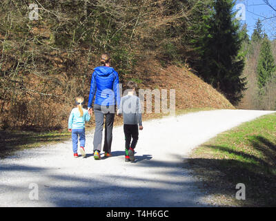 Madre e figlio e figlia escursionismo e divertirsi e beeing felici insieme e tenendo le mani. Viaggio di famiglia in una foresta a molla. Foto Stock