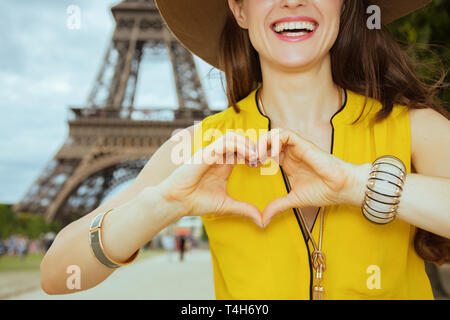 Primo piano su buon viaggiatore moderno donna in giallo camicetta e hat mostra a forma di cuore le mani contro la Torre Eiffel a Parigi, Francia. Foto Stock