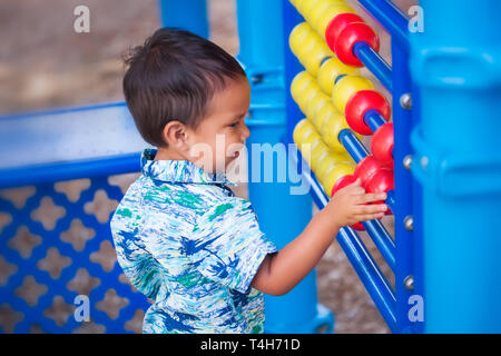 Un ispanico little boy imparare a contare con un enorme abacus in un parco giochi per bambini area. Foto Stock