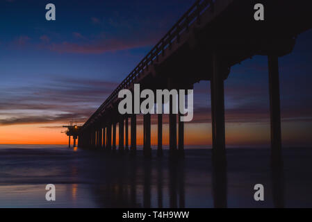 Brillante tramonto con il drifting le nuvole colorate con una silhouette del cemento Scripps Pier con la marea, La Jolla, San Diego, CA, Stati Uniti d'America. Foto Stock