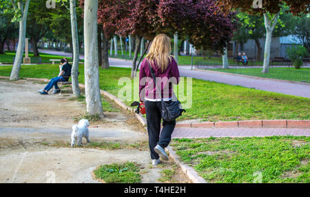 Donna bionda prende il suo cane per una passeggiata con un guinzaglio in un percorso al parco. Le donne a piedi cane a parchi in Murcia, Spagna, 2019 Foto Stock