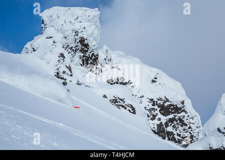 Sull'isola di Hokkaido, uno sciatore incisioni attraverso la polvere soffice neve come egli sci backcountry su un picco vulcanico con formazioni rocciose al di fuori di Niseko Foto Stock