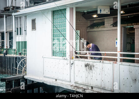 Pescatore non identificato al ponte del traghetto Star di Tsim Sha Tsui. Il pescatore cinese utilizza pesce pesca con la canna da pesca nel mare al Victoria Harbour Foto Stock