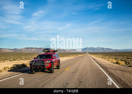 Red pickup truck caricato con overlanding e attrezzatura da campeggio. Il carrello è in marcia sull'autostrada extraterrestre vicino Area 51 nella vasta Nevad aperto Foto Stock