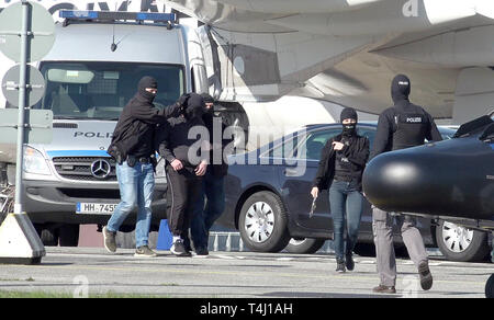 Amburgo, Germania. Xvii Apr, 2019. Un elemento di sospetto della milizia terroristica è (secondo da sinistra) è portato a un elicottero della polizia federale presso l'Aeroporto di Amburgo. Il piano sarà in grado di volare il sospetto di Karlsruhe, dove un giudice istruttore presso l'Alta Corte federale deciderà in merito all'esecuzione della detenzione in attesa di processo. Credito: Bodo segna/dpa/Alamy Live News Foto Stock