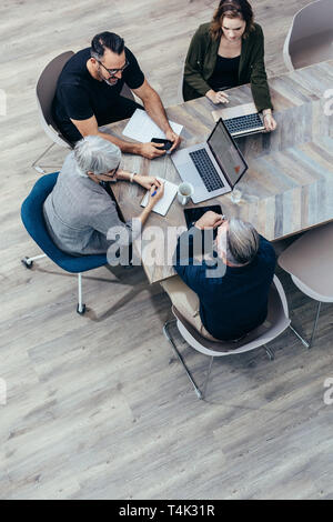 Vista superiore del team aziendale a discutere attorno ad un tavolo in ufficio. Un gruppo di persone di affari avente una riunione di brainstorming. Foto Stock