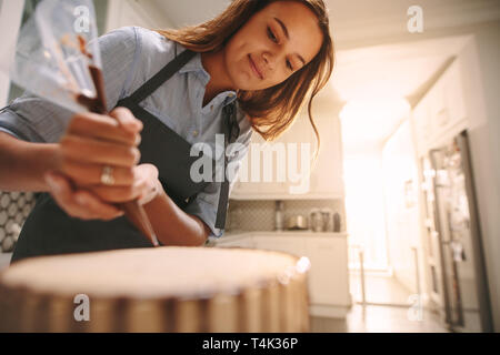 Femmina pasticcere decorare una torta al cioccolato in cucina. Donna che indossa un grembiule facendo una deliziosa torta a casa. Foto Stock