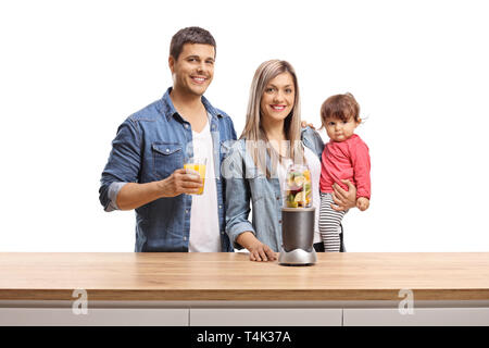 Madre, padre e un bambino in posa dietro un banco di legno con frutta in un frullatore isolati su sfondo bianco Foto Stock