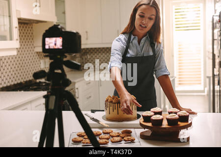 Social media influencer donna la registrazione di contenuti video in cucina, pasticceria mostra sul tavolo. Femmina riprese di pasticceria se stessa della sua cu online Foto Stock