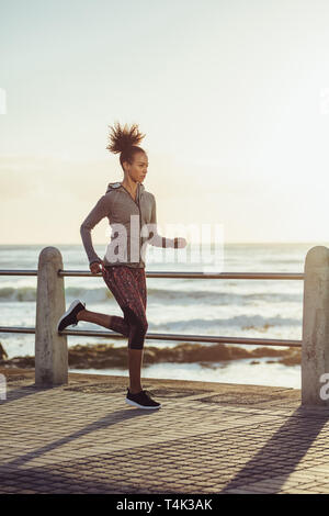 Montare la giovane donna di jogging sul lungomare. Vista laterale del femminile in una corsa al tramonto. Foto Stock