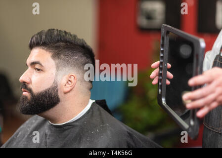 Bel uomo barbuto guardando nello specchio dopo il taglio di capelli, al Barber shop . Foto Stock