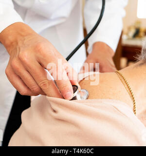 Primo piano di un medico caucasica uomo in camice bianco, auscultating senior caucasica donna paziente utilizzando uno stetoscopio, a casa sua o ad una assistenza infermieristica hom Foto Stock