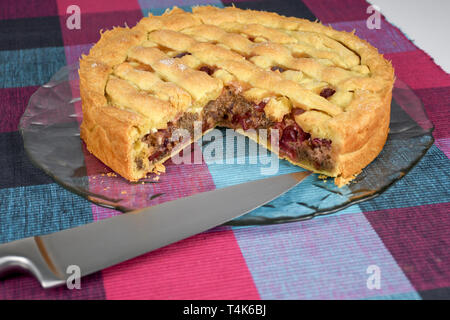 Sostenuto croccanti e dolci fatti in casa torta di ciliegie su una lastra di vetro e una tabella coperta con colorati cubo panno pattern close up Foto Stock