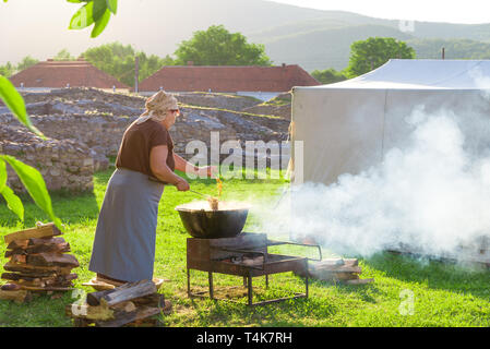 Donna rumena di cottura del cibo tradizionale sul fuoco all'aperto in vacanza in campeggio in stagione estiva Foto Stock