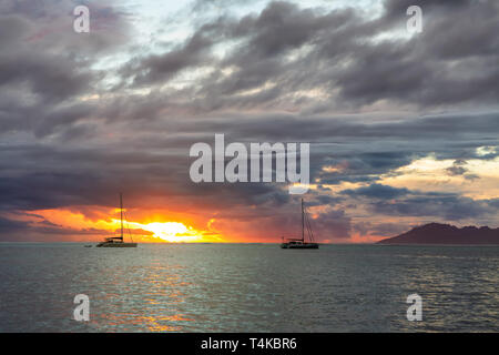 Due barche a vela sopra le nuvole scure e sfondo arancione tramonto mare Foto Stock