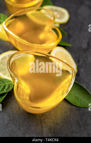 Limone giallo jelly nel cuore di vetro sagomato con tagliare fette di limone su sfondo scuro, composizione verticale, vista dall'alto Foto Stock