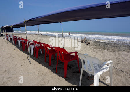 La tettoia ombreggiatura di una fila di sedie vuote su una spiaggia soleggiata Foto Stock