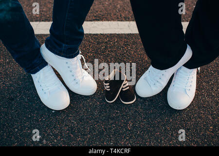 Ritagliato maschio e femmina gambe indossando sneakers bianco tra loro sono sneakers per il loro bambino Foto Stock