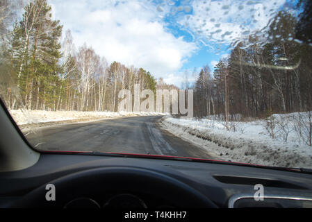 Vista della strada attraverso il parabrezza. Neve in disparte. Strada asfaltata bagnata. Il cielo blu con nuvole. Il punto di vista del guidatore guardando attraverso Foto Stock