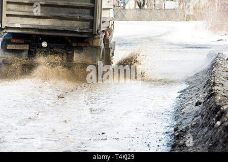 Onda sporca di spruzzo da sotto le ruote di un carrello. Acqua sulla strada. Foto Stock