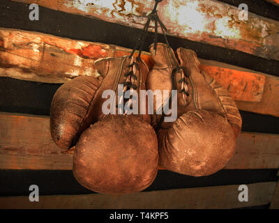 I guantoni sulla parete. Vecchio, vintage paio di guanti in pelle è appeso alla parete di legno. I colori rosso e luci soffuse. Guanti del boxer in pensione Foto Stock