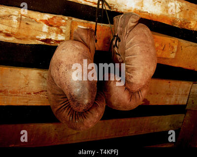 I guantoni sulla parete. Vecchio, vintage paio di guanti in pelle è appeso alla parete di legno. I colori rosso e luci soffuse. Guanti del boxer in pensione Foto Stock