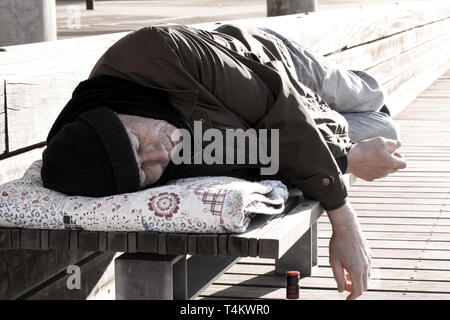 Uomo senza tetto o di rifugiato che dorme sul banco di legno Foto Stock