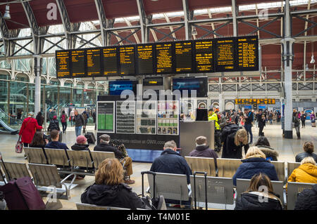 I viaggiatori in attesa mediante il display illuminato board presso la stazione di Paddington, Londra Foto Stock