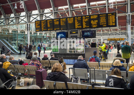 I viaggiatori in attesa mediante il display illuminato board presso la stazione di Paddington, Londra Foto Stock