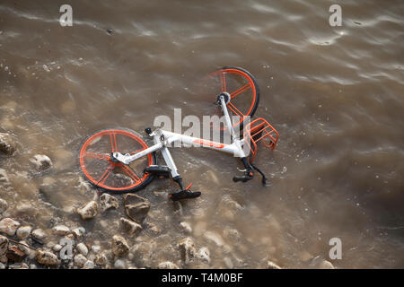 Acqua di fiume lambisce un scartato Mobike noleggio bici sul litorale gettato nel fiume Tamigi da vandali nei pressi di Westminster Bridge Foto Stock